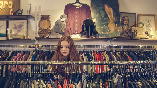 A young woman with long red hair browses a clothing rack in a store to find the perfect outfit for her acting headshots